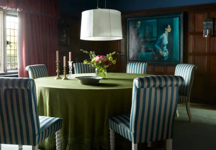 A dining room with a round green table, striped chairs, and a large painting. The table styles are classic and elegant.