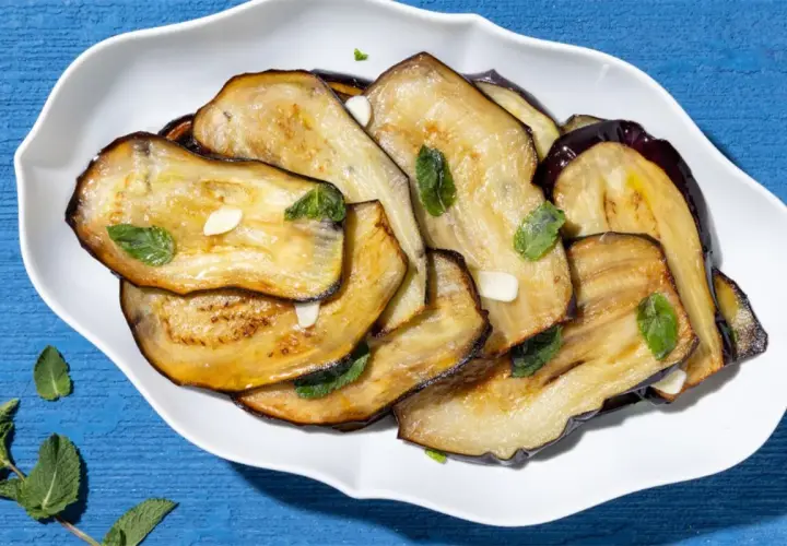 Fette di melanzane grigliate, guarnite con menta fresca e aglio. Un contorno di verdure semplice e gustoso.