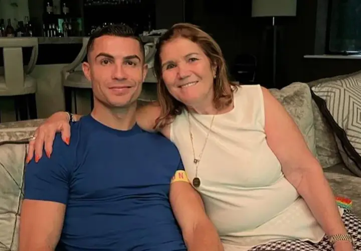 Cristiano Ronaldo z mamą, **Maria Dolores dos Santos Aveiro**, uśmiechają się do zdjęcia, siedząc na kanapie.