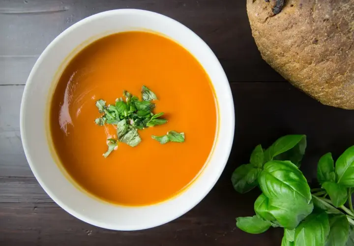 Pomidorowa zupa w misce, udekorowana bazylią, obok bochenek chleba. Zastanawiasz się, jak długo można przechowywać zupę w lodówce?