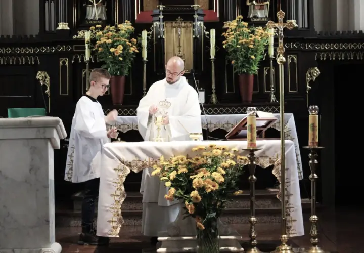 Ksiądz i ministrant podczas mszy świętej przy ołtarzu ozdobionym kwiatami.