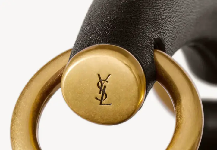 Złote logo YSL na czarnym pasku, element luksusowej torebki. YSL to francuski dom mody.