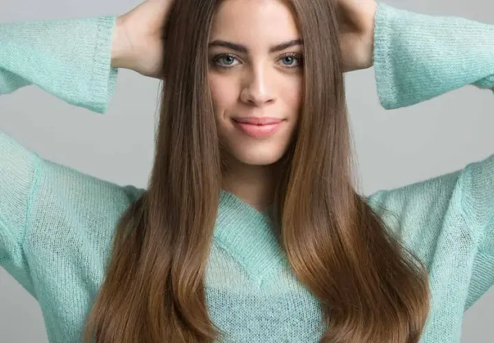 Joven sonríe con las manos en la cabeza, su cabello castaño cae sobre sus hombros. Apenas se notan las primeras canas, un toque de madurez.