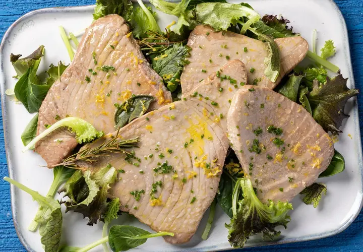 Fette di tonno al forno, profumate al limone e erbe aromatiche, servite su un letto di insalata fresca.