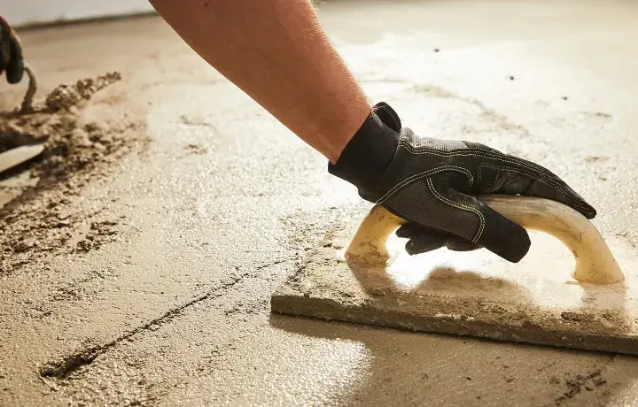 Arbeiter verlegt Estrich mit Glättkelle. Der frische Estrich wird sorgfältig bearbeitet, um eine ebene Fläche zu schaffen.