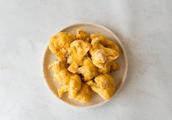 Alitas de coliflor doradas y crujientes en un plato, listas para disfrutar.