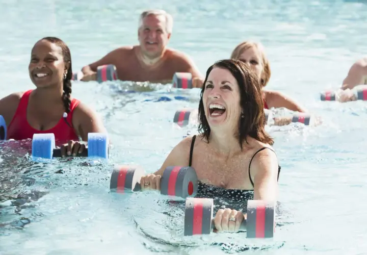 Personas sonriendo y haciendo aqua gym en una piscina con pesas flotantes.