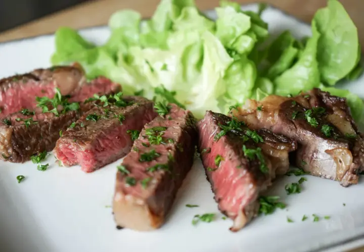 Tranches de steak black angus saignant, garnies de persil frais, servies avec de la laitue croquante sur une assiette blanche.