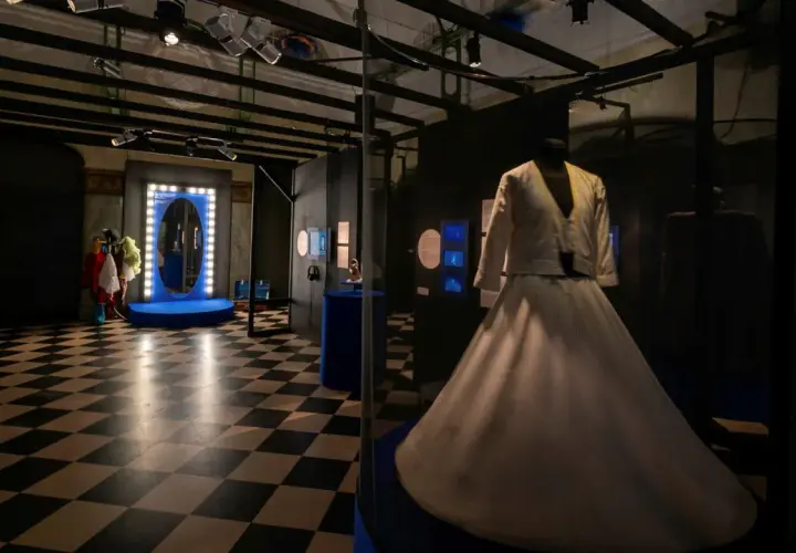 En vit dansklänning visas upp i en monter på Dansmuseet Stockholm. Golvet har ett schackrutigt mönster.