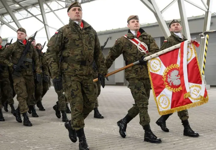 Żołnierze w mundurach maszerują z flagą. Uroczysta przysięga wojskowa w pełnym rynsztunku.