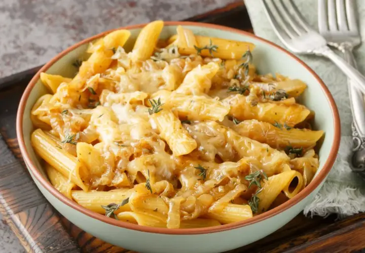 Makaron penne z karmelizowaną cebulą i roztopionym serem, ozdobiony tymiankiem.