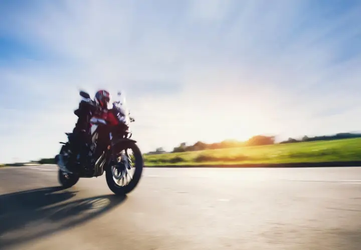 Motocyklista w kasku pędzi drogą, ciesząc się pięknym zachodem słońca. To idealny **sezon motocyklowy**!
