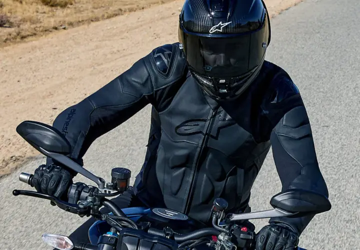 Motocyklista w kasku i czarnej kurtce Alpinestars jedzie po pustynnej drodze.