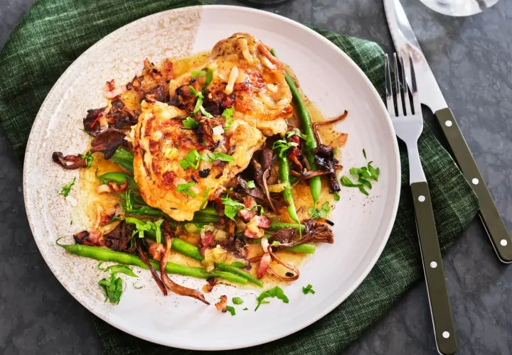 En tallrik med kyckling i vitvinssås, svamp, haricots verts och bacon. En utsökt coq au vin blanc.