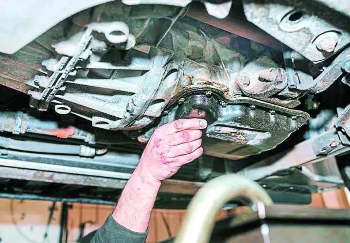 Mano revisa el cárter de un coche, mostrando signos de perdida de aceite.
