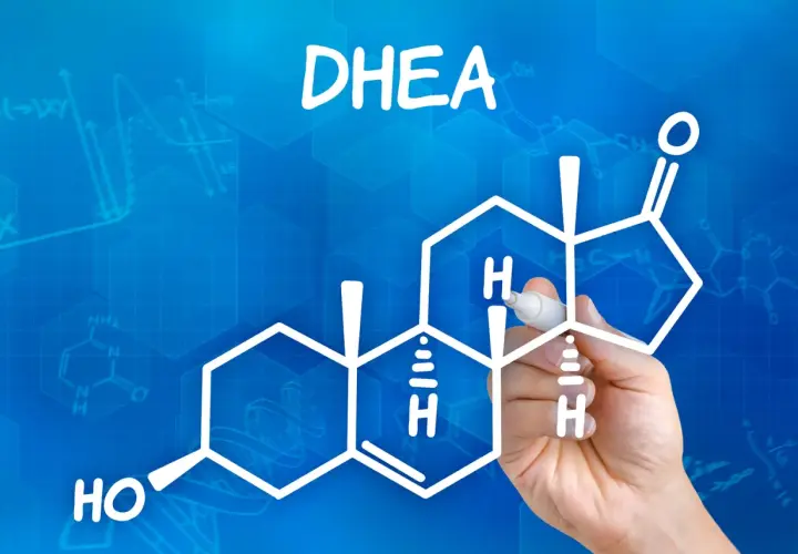 DHEA co to? Rysunek przedstawia wzór chemiczny DHEA, hormonu steroidowego, z ręką piszącą markerem.