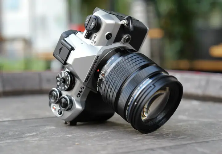 Srebrny aparat OM SYSTEM OM-5 z obiektywem M.ZUIKO DIGITAL 12-45mm 1:4, gotowy do uchwycenia każdej chwili.