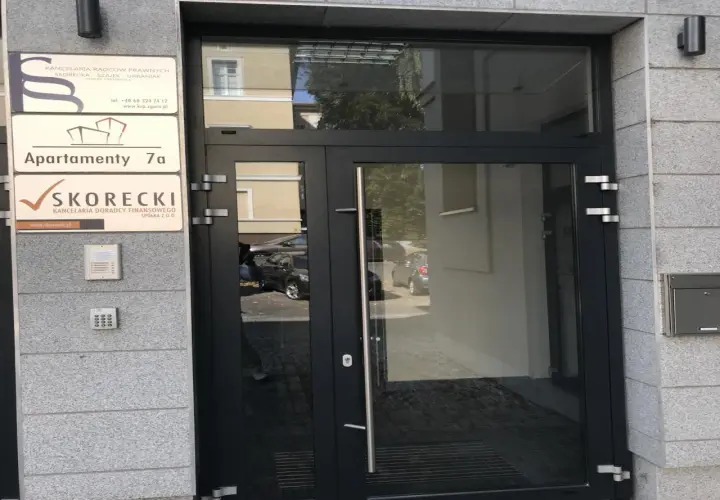Drzwi wejściowe do budynku z tabliczkami informacyjnymi, w tym "SKORECKI KANCELARIA DORADCY FINANSOWEGO".