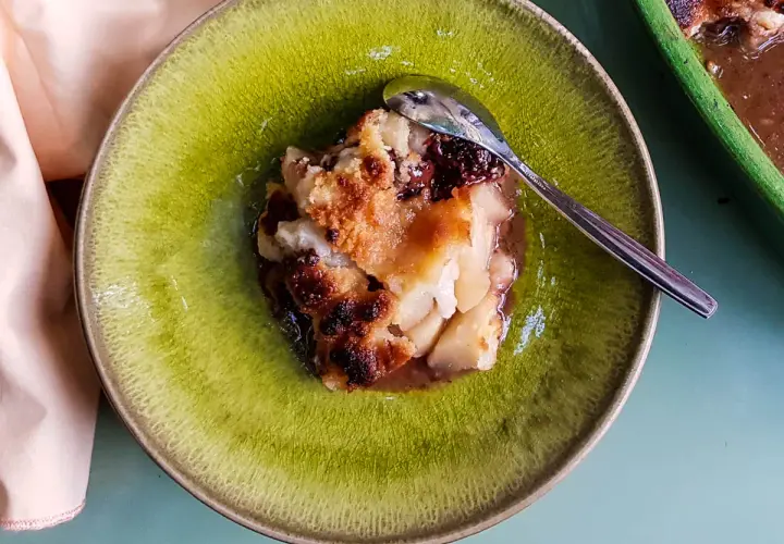 Un délicieux crumble poire chocolat, doré et croustillant, servi dans une assiette verte avec une cuillère.