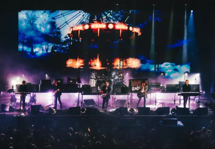 The Cure Polska na żywo. Zespół gra na scenie, w tle wielki ekran z karuzelą.