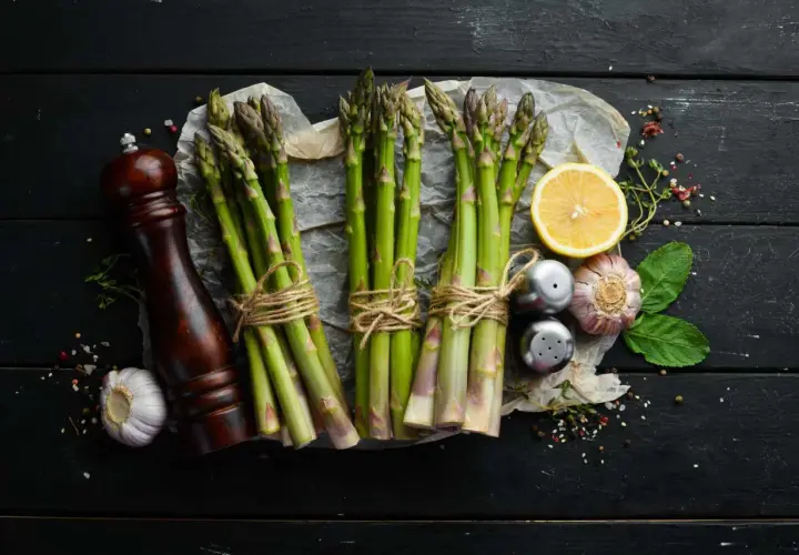 Des asperges fraîches, citron, ail et moulin à poivre sur fond noir. Idéal pour savoir quel vin avec asperges.