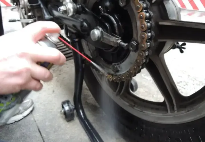 Mano spruzza spray sulla catena della moto per pulirla.