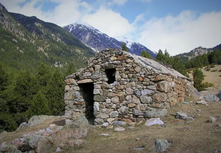 Antigua cabaña de piedra en el Vall de la Llosa, rodeada de pinos y montañas nevadas.