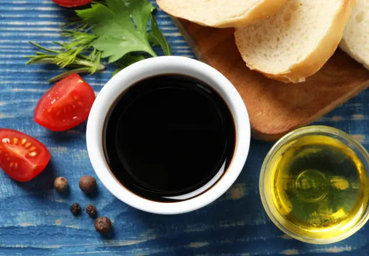 Sos do czego? Ocet balsamiczny, oliwa, pomidorki i pieprz na niebieskim tle. Idealne składniki na pyszną sałatkę.
