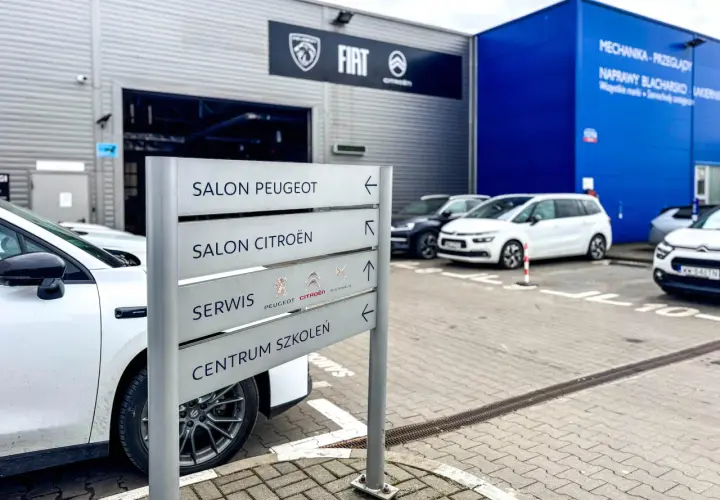 Znak z napisem "Salon Peugeot", "Salon Citroën", "Serwis" i "Centrum Szkoleń" przy salonie samochodowym. ASO skrót.