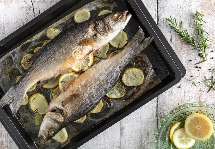 Due branzini al forno su teglia con patate, limone e rosmarino. Un piatto semplice e gustoso pronto per essere servito.