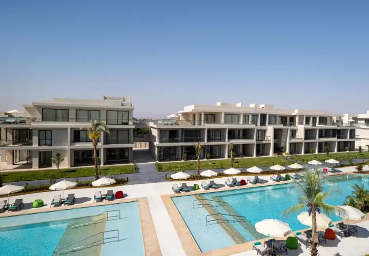 Nowoczesne budynki hotelowe Rixos z basenami i leżakami pod palmami.