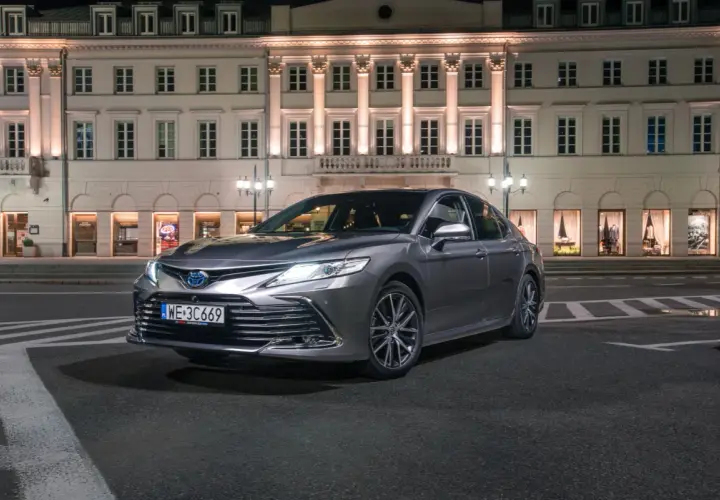 Elegancka, szara Toyota Camry 2024 zaparkowana nocą przed zabytkową kamienicą.