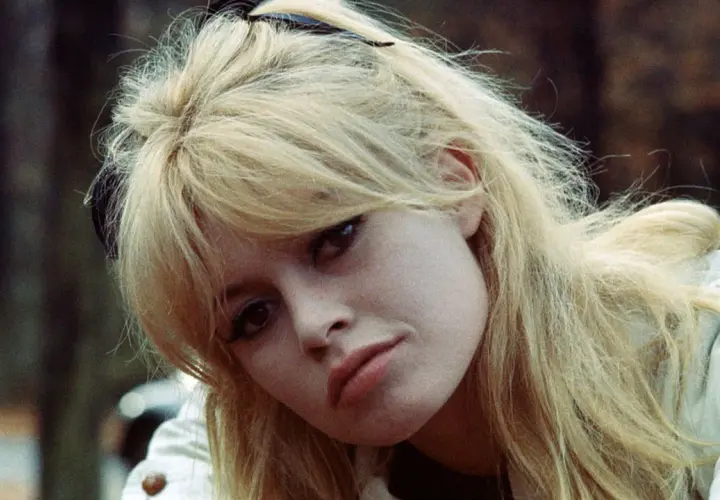 Blonde Frau mit langen Curtain Bangs, die leicht zerzaust sind. Ihr Blick ist nach unten gerichtet.