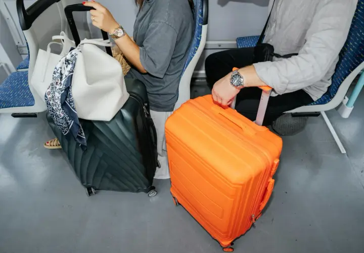 Podróżni z bagażami: duża pomarańczowa walizka i ciemnozielona, obok biała torba. Jaki bagaż do samolotu?