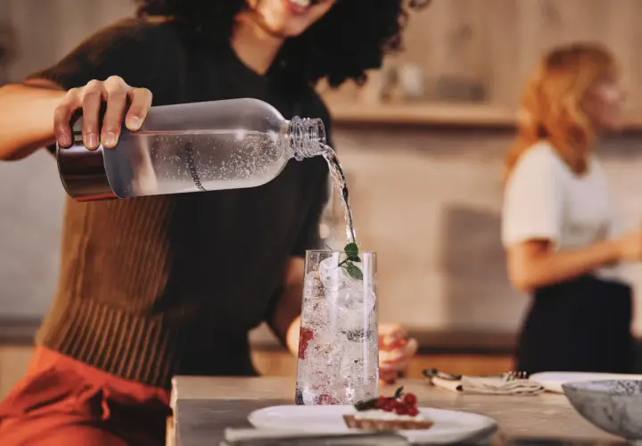 Przygotowanie efektownej kolacji dla znajomych. Nalewanie wody do szklanki z lodem i owocami.