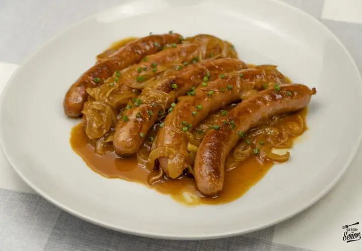 Salchichas doradas en salsa de cebolla caramelizada, un plato delicioso para aprender como hacer salchichas caseras.