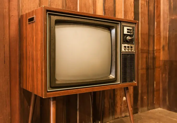 Stary telewizor z drewnianą obudową i ekranem, jak pierwszy telewizor, stoi na tle drewnianej ściany.