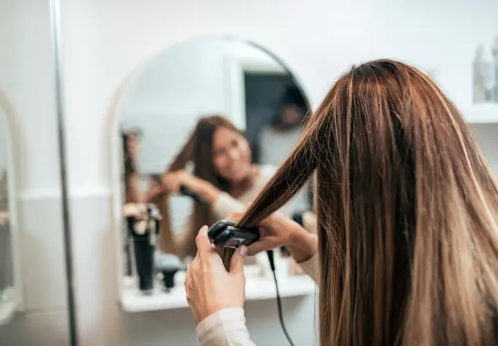 Mujer se alisa el pelo mojado frente al espejo.