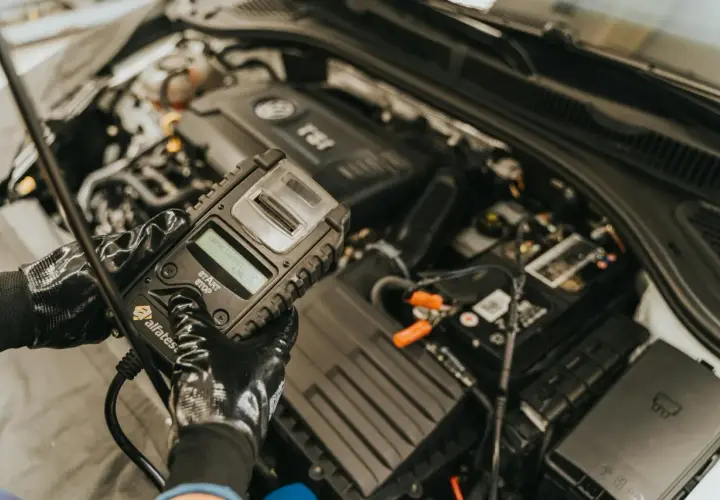 Mechanik w rękawiczkach sprawdza stan akumulatora za pomocą testera, który może również diagnozować czujnik halla w samochodzie.