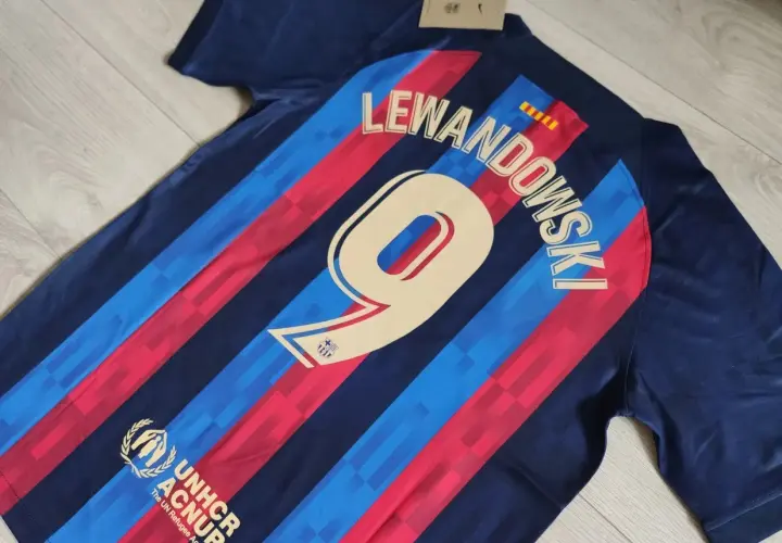 Koszulki meczowe FC Barcelona z nazwiskiem Lewandowskiego i numerem 9. Widoczny też herb UNHCR.