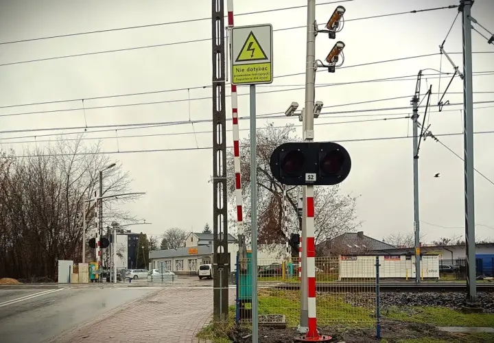 Kamery na przejazdach kolejowych monitorują bezpieczeństwo. Na zdjęciu widać sygnalizację świetlną, rogatki i kamery nadzorujące.