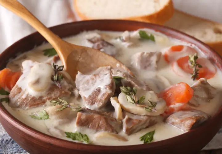 Un réconfortant blanquette de veau facile, servi dans un bol en bois avec une cuillère, garni de persil et de thym.