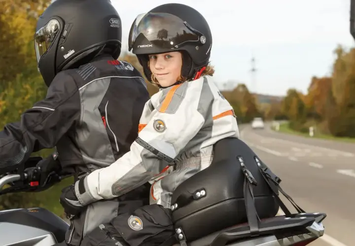 Dziecko w kasku z uśmiechem siedzi z przodu motocykla, gotowe na wspólną podróż. Przewożenie dziecka na motocyklu to przygoda!