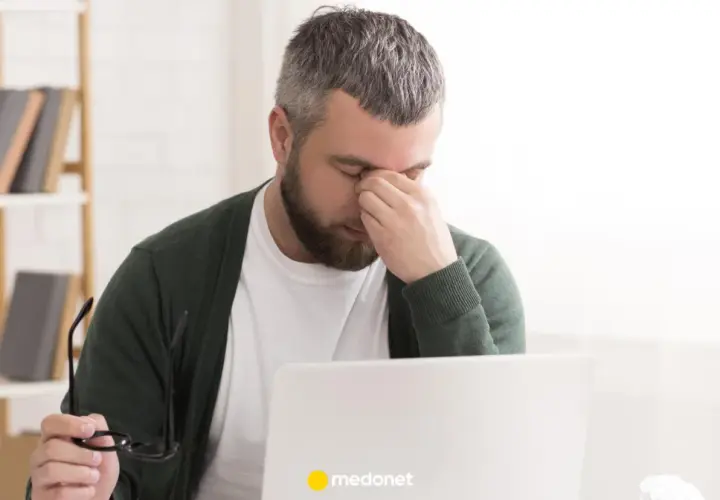 Mężczyzna z zespołem pustego siodła masuje oczy, siedząc przy laptopie.