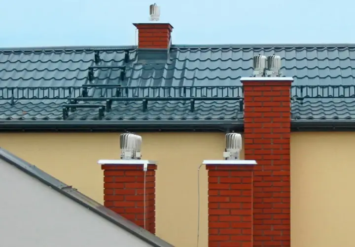 Dwa ceglane kominy z obrotowymi nasadami zapewniają sprawną wentylację w domu.
