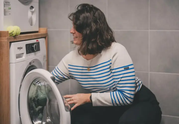 Kobieta w paski wkłada ubrania do pralki. Dowiedz się, jak prać odzież termoaktywną, by służyła latami.