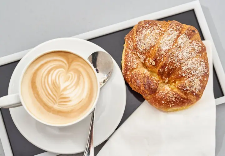 Cappuccino con latte art e brioche americane cosparse di zucchero.
