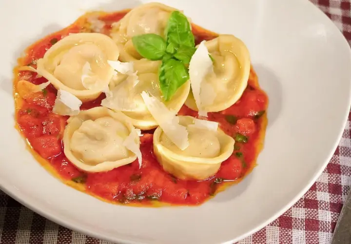 Pyszne ravioli z szynką parmeńską w sosie pomidorowym, posypane parmezanem i udekorowane bazylią.