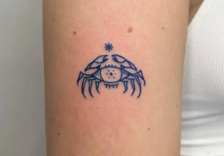 Niebieski tatuaż raka z okiem w środku, symbolizujący intuicję i ochronę.