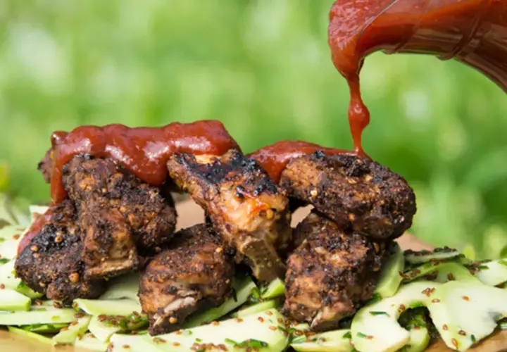 Grillade revbensspjäll toppas med en generös mängd röd bbq sås, serverade på en bädd av gurksallad.